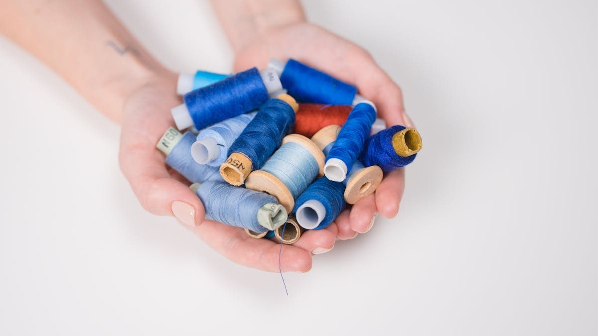 A close-up shot of diverse colorful sewing threads held in hands against a white background.